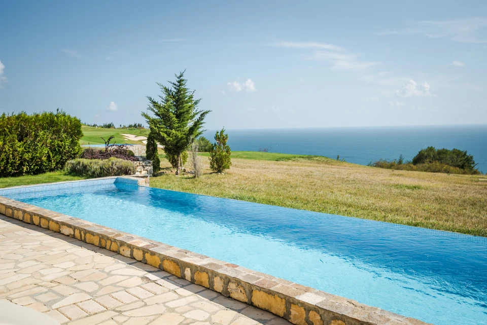 Piscine à débordement extérieure avec margelles en pierre naturelle et parement en moellons dorés, située sur terrain paysager face à la mer