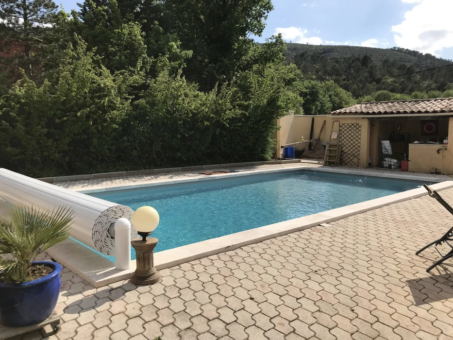 Piscine extérieure rectangulaire avec couverture automatique à enrouleur, située dans jardin paysagé avec montagnes boisées en arrière-plan