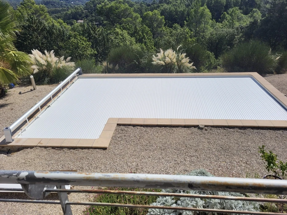 Piscine rectangulaire extérieure avec couverture à barres automatique déployée, entourée de margelles en pierre claire