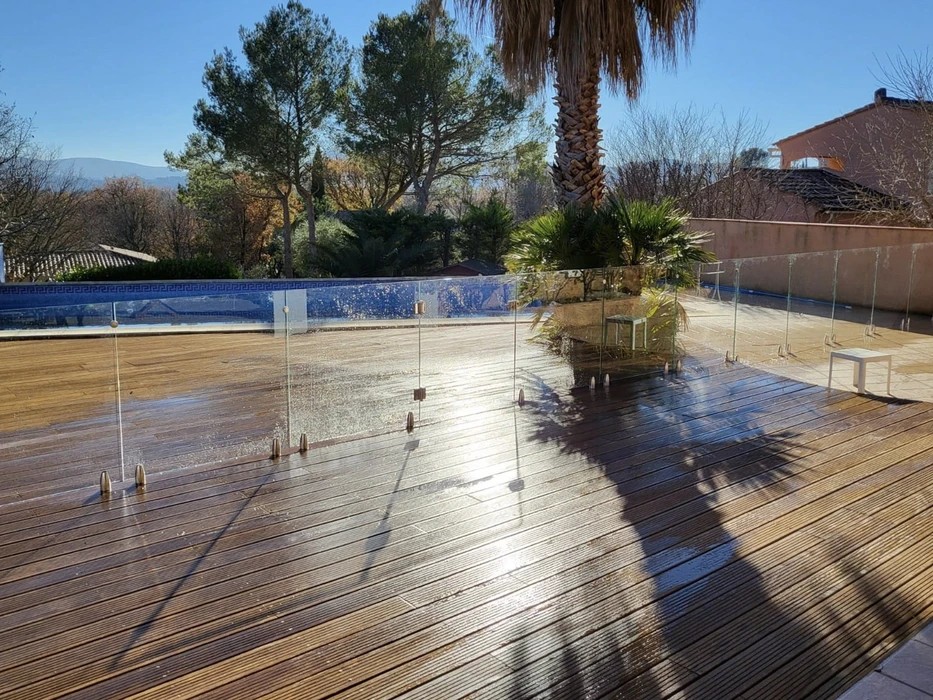 Terrasse extérieure ensoleillée avec piscine carrelée bleue et garde-corps en verre transparent