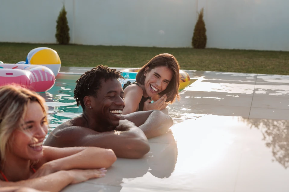 Mère et fille nageant dans une nouvelle piscine arrière avec chien un patio de pavés et de pelouse et jardins verts