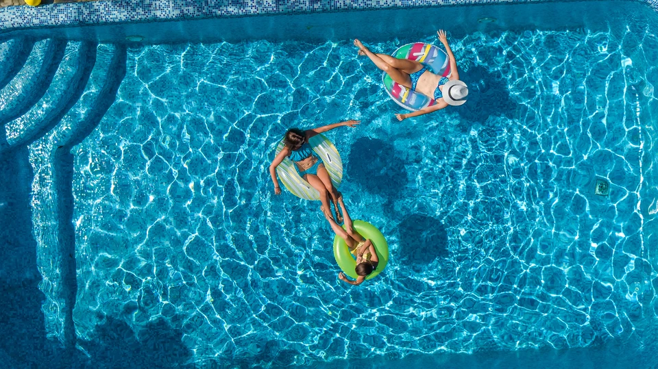 Enfant avec brassards jaunes nageant dans piscine extérieure avec vue panoramique sur montagnes enneigées