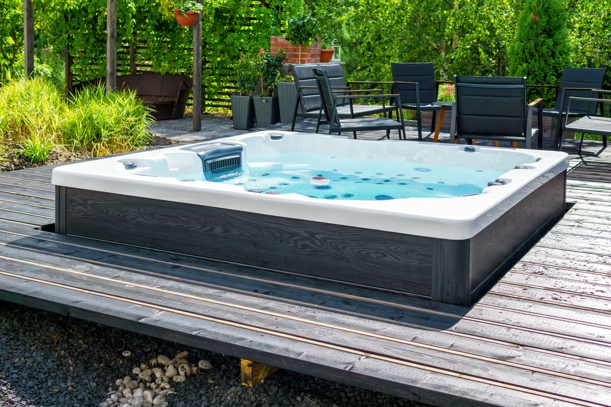 Scène extérieure sur terrasse en bois avec spa jacuzzi rectangulaire blanc à jets multiples, installé sur deck