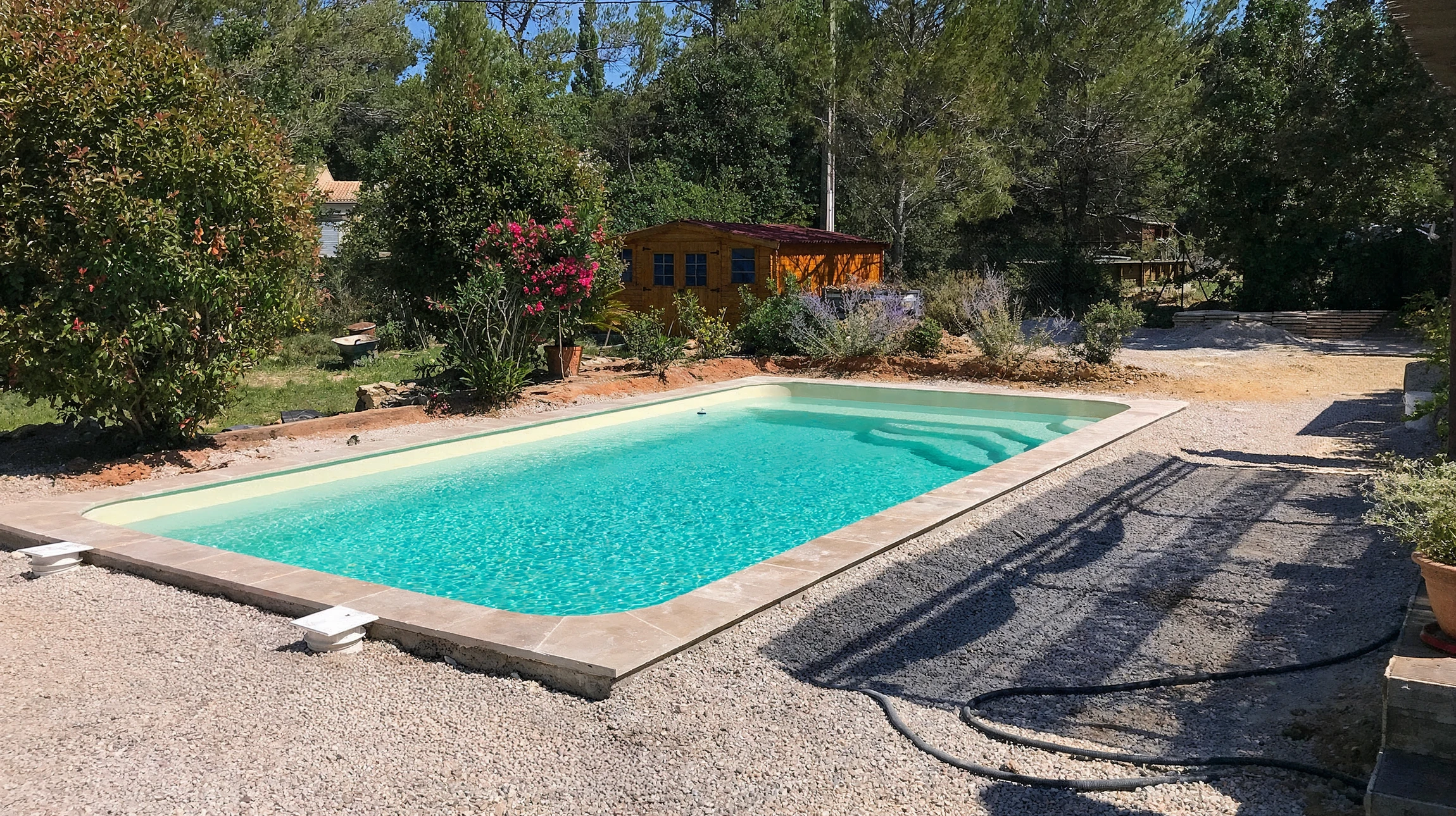 Aménagement extérieur nocturne avec piscine rectangulaire éclairée en bleu, entourée de margelles en composite anthracite