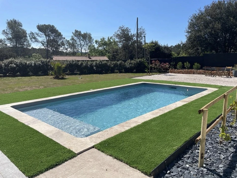 Piscine rectangulaire extérieure avec margelles en pierre naturelle, située dans jardin paysagé avec gazon synthétique