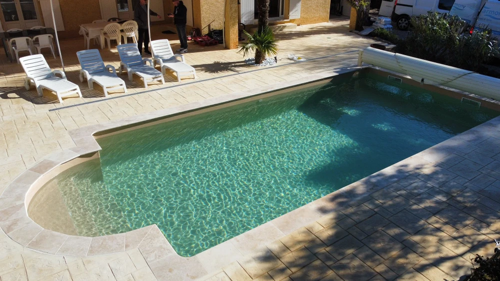 Piscine moderne extérieure avec margelles en pierre naturelle claire, bassin aux eaux bleu-vert, débordement à l'anglaise