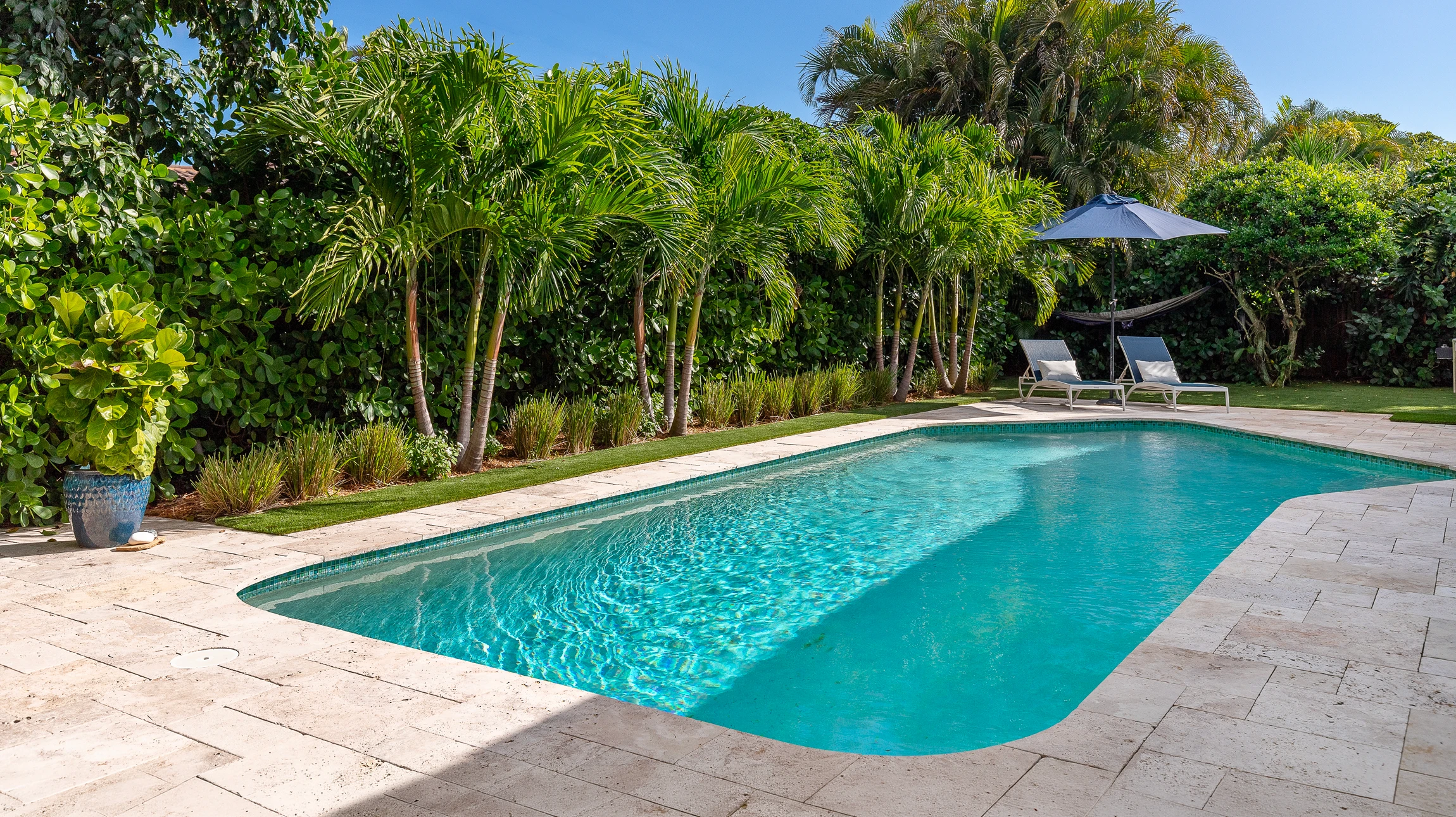 Piscine résidentielle avec cage d'écran sous ciel bleu, située face à un canal avec maisons et bateaux