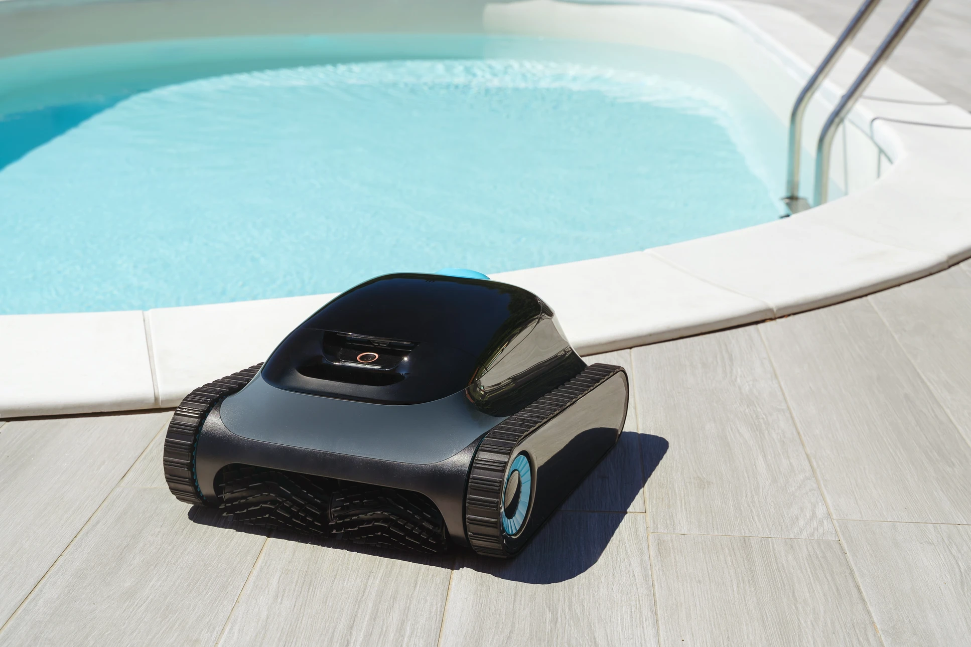 Piscine extérieure avec robot nettoyeur automatique bleu posé sur margelle en pierre